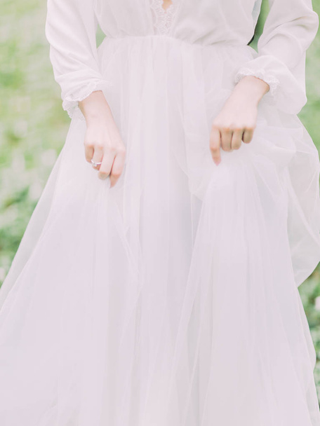 The front photo of the hands of woman holding the white wedding dress at the green background. - Fotografie, Obrázek
