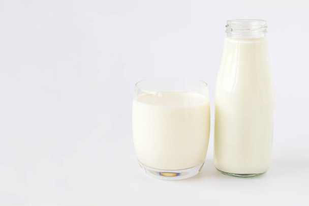 Fles melk en glas melk op een witte achtergrond - Foto, afbeelding