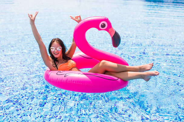 Beauty girl sits on inflatable mattress flamingos in the pool - Fotó, kép