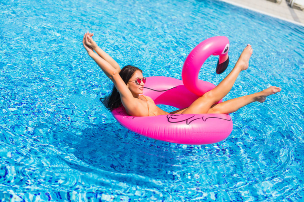 Belle femme, en maillot de bain, couchée sur un matelas gonflable rose flamant rose dans une piscine d'eau bleue, été
 - Photo, image