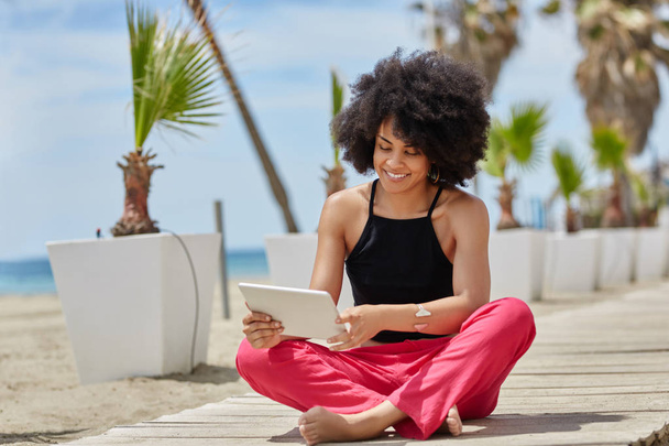 Happy afro american woman sitting crossed legs using tablet - 写真・画像