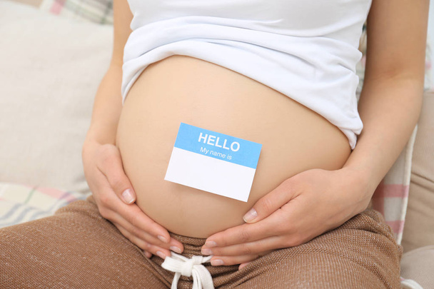 Pregnant woman with paper sticker on tummy, closeup. Concept of choosing baby name - Foto, Imagem