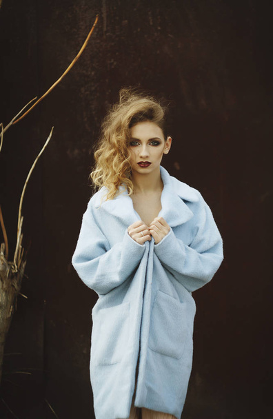 Young beautiful blonde woman posing in blue coat outdoors - Photo, image