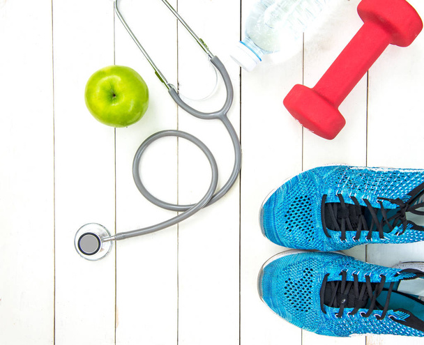 Diet and weight loss for healthy care with medical stethoscope, fitness equipment,measuring tap,fresh water and green apple on wooden background top view.  Healthy Concept. - Fotografie, Obrázek