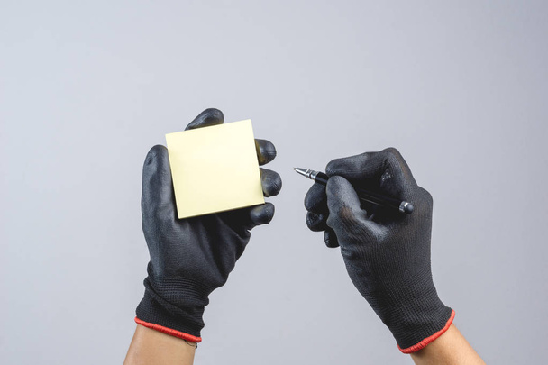 Hand wearing dark glove and holding pen and sticky paper note as - Photo, Image