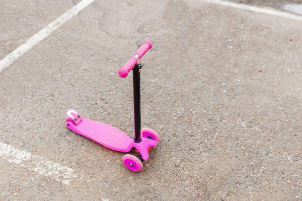 Pieni vaaleanpunainen skootteri lapsille asfaltin jalkakäytävällä
 - Valokuva, kuva