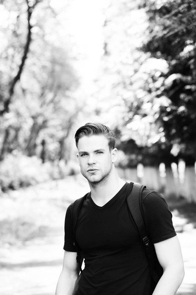 Man with stylish hairdo, sportive outfit, black backpack in park - Fotó, kép