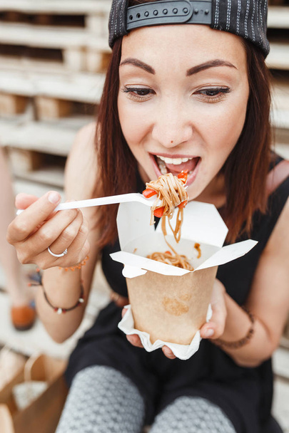 Joven mujer comiendo wok asiático fideos cocina de llevar caja en el fondo urbano de la calle
 - Foto, imagen
