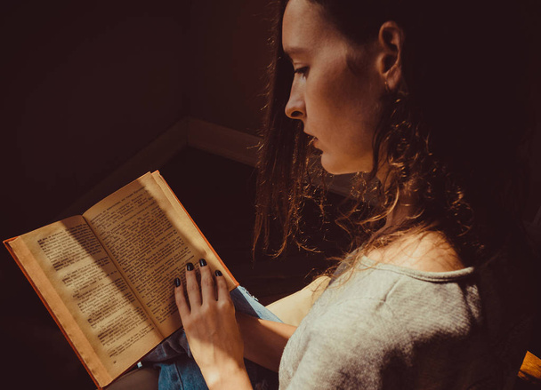 Spending free time by reading books. Girl preoccupied with reading old interesting paper book. Natural light. Enjoy morning. Warm atmosphere. Knowledge, learning and education concept. Woman bookwarm. - Foto, Imagem
