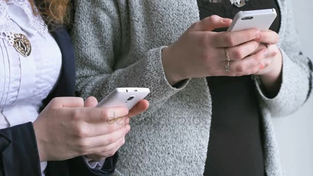 Schoolgirls hold smart phones in hands indoors - Filmati, video