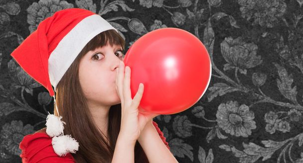 woman wearing a christmas hat and blowing a balloon - Φωτογραφία, εικόνα