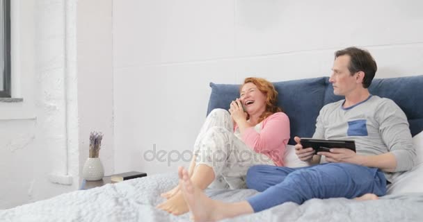 Jealous Man Looking At Woman Talking On Cell Phone Call Laughing Sitting On Bed In Couple Bedroom - Πλάνα, βίντεο