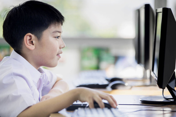 学生制服の学校でコンピューターを使用してのアジアの少年の幸せ . - 写真・画像