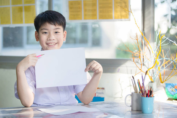 Feliz asiático chico mano celebración en blanco A4 hoja de papel y mirando
 - Foto, Imagen