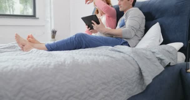 Coupe Sitting On Bed Using Digital Tablet Computer, Embracing Man And Woman Talking In Bedroom Browsing Internet - Filmati, video