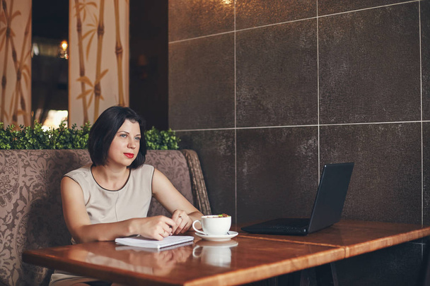 Young caucasian businesswoman with laptop and notebook. Woman in cafe - 写真・画像