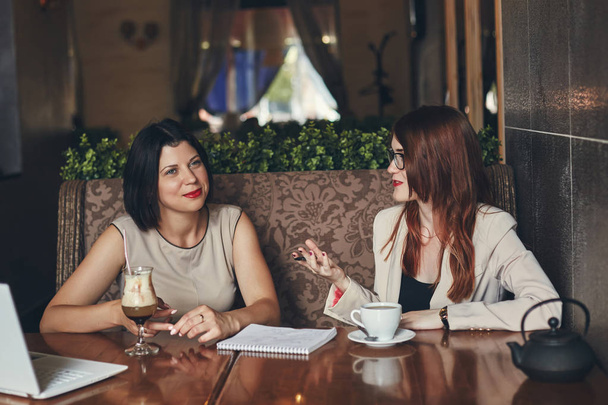 Two young smiling caucasian businesswomen with laptop. Women in cafe - Фото, зображення