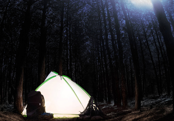 Nachtwald mit Rucksackausrüstung und beleuchtetem Zelt. - Foto, Bild