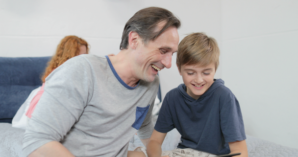 Happy Father And Son Use Tablet Computer Laugh Sitting On Bed In Bedroom Spending Time Together - Πλάνα, βίντεο