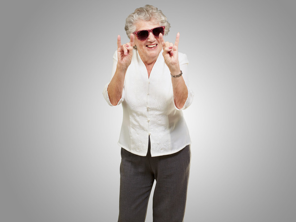 ritratto di una donna anziana felice che fa il simbolo della roccia sopra il bac grigio
 - Foto, immagini
