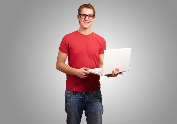 retrato de un joven estudiante sosteniendo el ordenador portátil sobre fondo gris
 - Foto, imagen