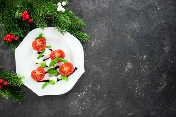Caprese salad in the shape of Christmas tree. Festive snack on dark background. Christmas table setting concept with salad dish - Photo, Image