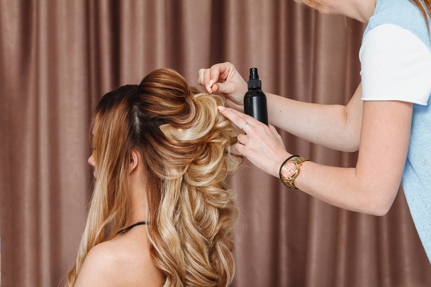 Closeup view of a hairdresser coiffeur makes evening hairstyle to the blond model in salon - Photo, Image