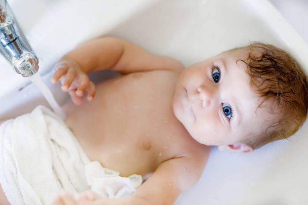Bebê adorável bonito tomando banho na pia de lavagem e pegar torneira de água
. - Foto, Imagem