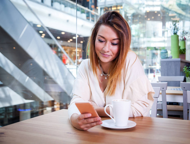 Dziewczyna przy użyciu telefonu komórkowego w kawiarni w centrum handlowym - Zdjęcie, obraz