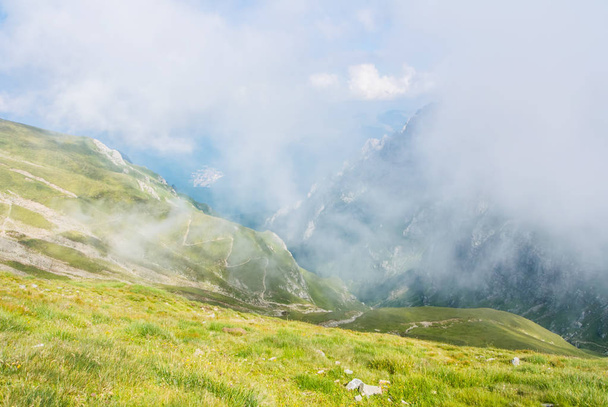 Panoramic view over the Carpatian mountains, serpentine path and a big fog cloud at the background, Bucegi natural park, Romania, on sunny summer day. - Photo, image