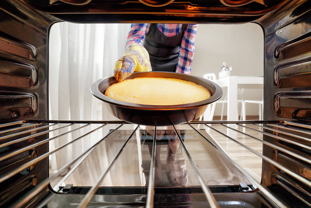 Housewife taking cheesecake out of oven in kitchen - Valokuva, kuva