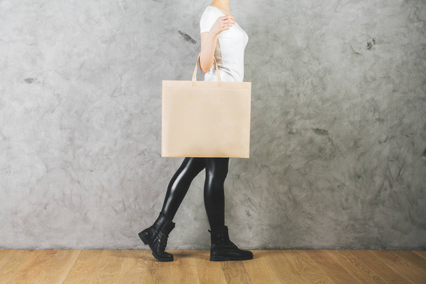 Woman holding empty shopping bag on concrete wall background. Merchandise concept. Mock up  - Photo, Image