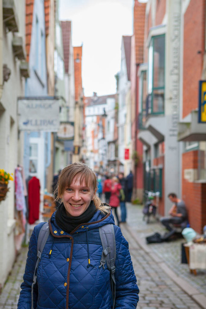 Jovem sorridente mulher turista sorrindo com casas coloridas no histórico Schnoorviertel em Bremen, Alemanha, ao fundo
 - Foto, Imagem