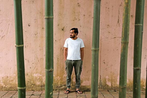 asiático hombre de pie en la pared con tener bambú árbol en frente de
. - Foto, Imagen