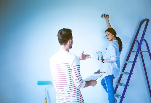 Portrait of happy smiling young couple painting interior wall new house - Foto, afbeelding