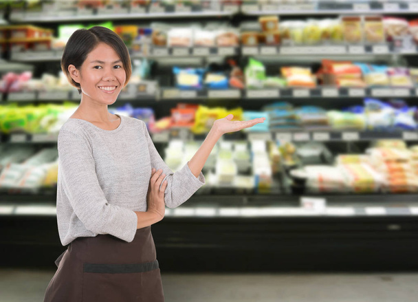 スーパー マーケットの棚に立っている笑顔の女性従業員  - 写真・画像