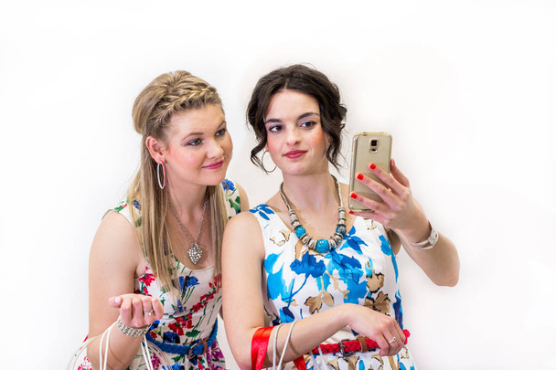 Dos jóvenes amigos con brillantes vestidos de verano tomando fotos con el teléfono inteligente móvil
. - Foto, imagen