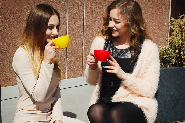 Дві молоді досить щасливі жінки сидять на відкритому повітрі і п'ють каву
 - Фото, зображення