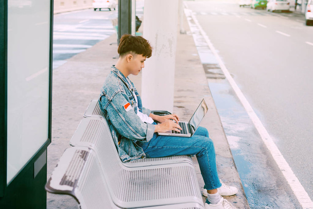 Asian young man sitting on the chair at the airport bus stop and - Φωτογραφία, εικόνα