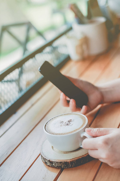 Mujer usando teléfono inteligente con una taza de café en la cafetería cafetería con fondo de filtro de color vintage
 - Foto, Imagen