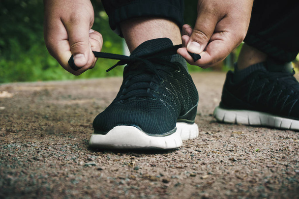 Urheilija sitoo kengännauhat lenkkarit ennen harjoittelua ulkona
 - Valokuva, kuva
