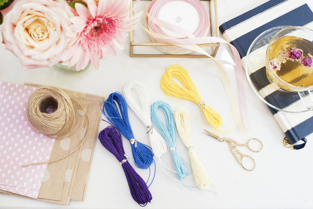 Handmade, craft concept. Materials for making string bracelets and handmade goods packaging - twine, ribbons. Feminine workplace concept. Freelance fashion femininity workspace in flat lay style with  - 写真・画像
