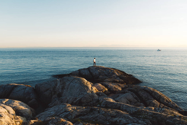 Uomo in piedi su rocce vicino alla spiaggia mentre il tramonto
  - Foto, immagini
