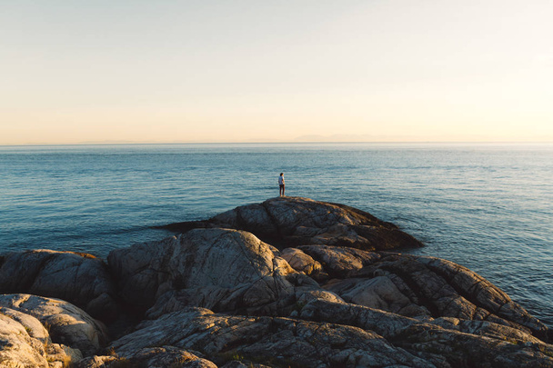 Ο άνθρωπος που στέκεται πάνω σε βράχια κοντά στην παραλία, ενώ ηλιοβασίλεμα  - Φωτογραφία, εικόνα