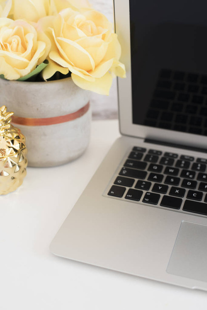 Feminine workplace concept. Freelance workspace with laptop, flowers, golden pineapple. Blogger working. Bright, yellow and gold. Vertical Styled stock photo - 写真・画像