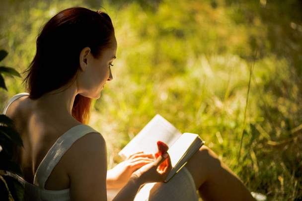 Young foxy haired woman reading book in nature. - Foto, Imagem