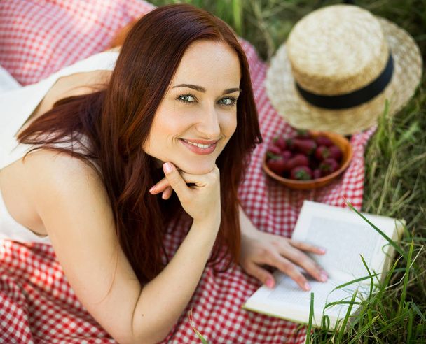 Charming young woman lies on cover on grass, reading book. - Foto, Imagem