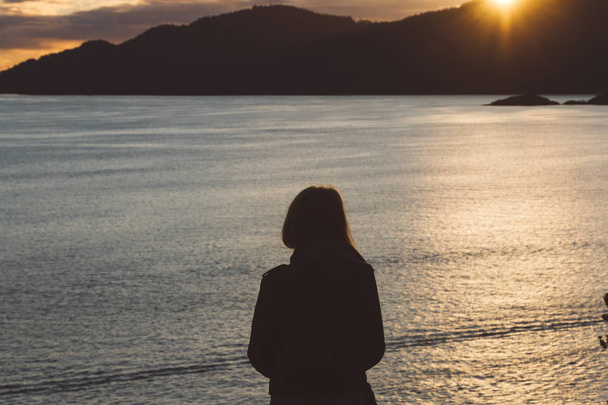 Silhouette einer Frau an der Küste mit Meer und Bergen während Sonnen - Foto, Bild