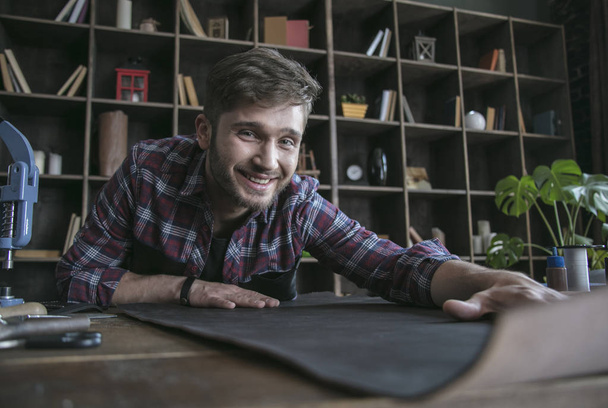 Young leather maker start work with smile on face and keep leather on table - Zdjęcie, obraz