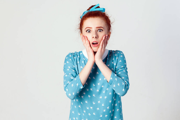 Human face expressions and emotions. Redhead young girl screaming with shock, holding hands on her cheeks. Isolated studio shot on gray background. - Photo, Image